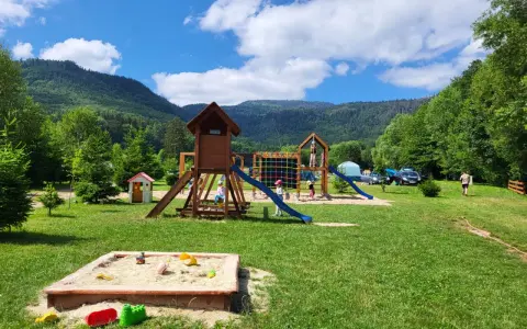Plac zabaw dla dzieci na terenie radków camping. Piaskownica, zjeżdżalnie i drabinki w otoczeniu zieleni i gór.