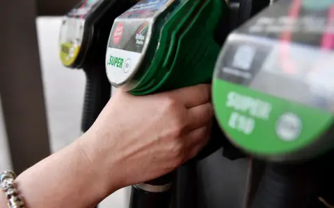 Hand greift nach Zapfhahn. Der steigende CO2-Preis macht sich beim Tanken bemerkbar.