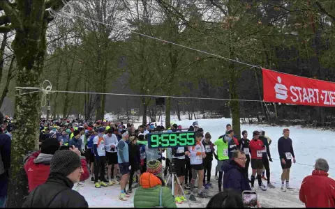 Läufer warten am Start-Ziel-Bogen für einen ultra marathon. Eine digitale Uhr zeigt 9:59:55.