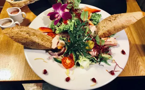 Kolorowy, świeży sałatka z rybą, pieczywem i kwiatem orchidei. Idealna propozycja, co zjesc w Jeleniej Górze.