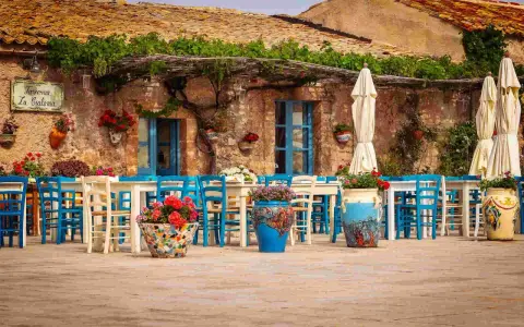 Taverna La Cialoma, un angolo incantevole di Siracusa e dintorni, con tavoli apparecchiati e sedie blu sotto un pergolato fiorito.