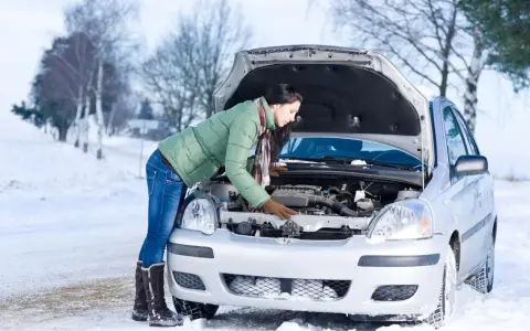 Kobieta w zimowej kurtce sprawdza silnik samochodu na śniegu. Zastanawia się, w jakiej temperaturze zamarza diesel, by uniknąć problemów.