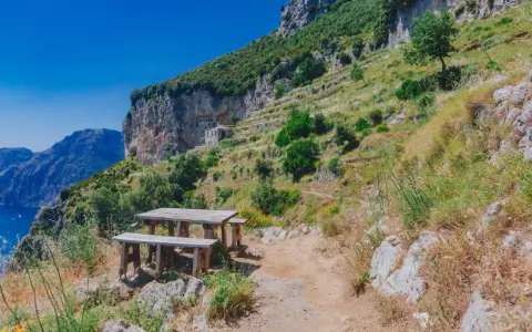 Un tavolo di legno su un sentiero roccioso, con una vista mozzafiato sul mare e sulle montagne. Un luogo perfetto per una pausa durante il cammino degli dei.