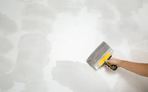 Mano con espátula aplicando masilla para alisar la pared, un paso clave en cómo quitar el gotele con espátula.