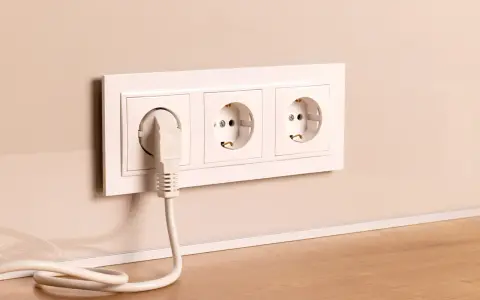 Prise électrique blanche avec un câble branché, installée à la hauteur du plan de travail.