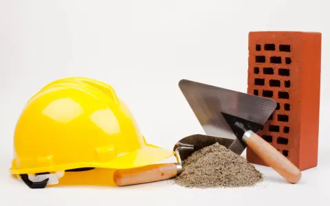 Casque jaune, brique rouge, tas de sable et truelles : les outils maçon essentiels pour bâtir.
