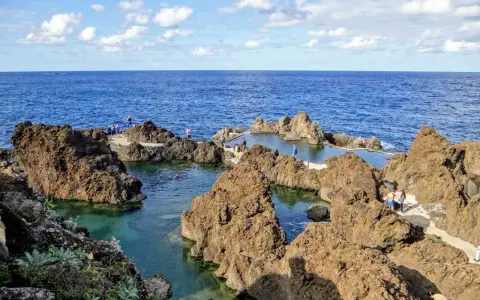 Naturschwimmbecken auf Madeira, umgeben von vulkanischem Gestein, mit Menschen, die die Sonne und das Meer genießen.