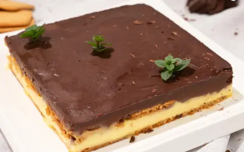 Deliciosa tarta de la abuela con capas de galleta y crema, cubierta de chocolate y decorada con menta fresca.