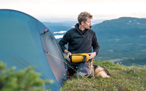 Man med hund packar för vandring. En gul sovsäck ligger redo. Perfekt packlista vandring dagstur.