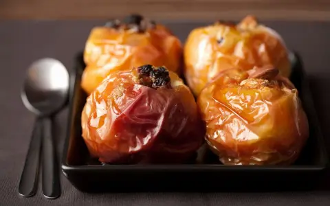 Mele cotte in friggitrice ad aria, caramellate e ripiene di uvetta e mandorle, pronte per essere gustate con un cucchiaio.