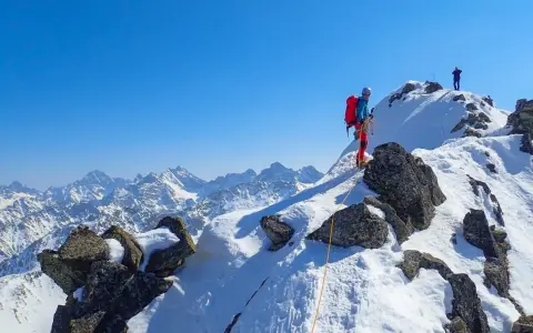 Zimowa wyprawa na Orlą Perć. Dwóch alpinistów wspinających się po ośnieżonych skałach, pod błękitnym niebem.