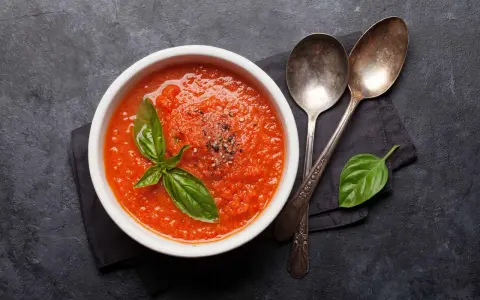 Eine Schüssel mit leckerer, italienischer Tomatensauce, garniert mit Basilikum und Pfeffer. Daneben liegen zwei Löffel.