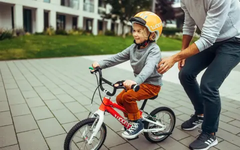 Chłopiec w kasku na rowerze, rozmiar 128, uczy się jeździć. Tata go asekuruje.