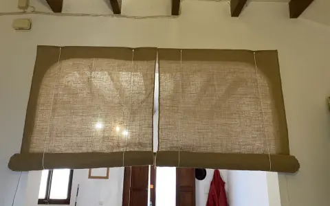 Dos estores enrollables caseros de tela de yute cubren una ventana y una puerta.