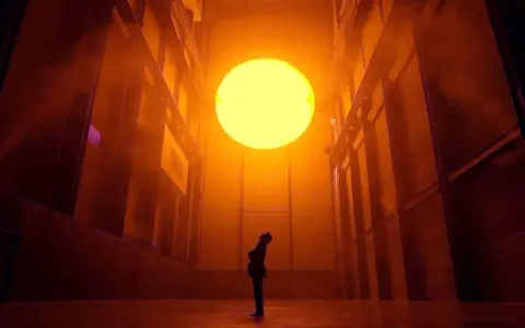Une personne contemple un soleil artificiel dans l'installation "The Weather Project" d'Olafur Eliasson, baignant l'espace d'une lumière orangée intense.