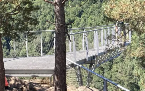 La passerelle himalayenne de Grazac offre une vue imprenable sur la vallée verdoyante. Une personne marche sur la structure métallique.