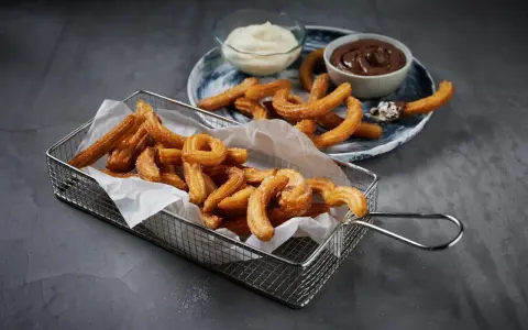 Krispiga churros i korg med chokladsås och grädde. Perfekt för ett enkelt churros recept hemma.