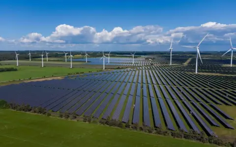 Großes Feld mit Windkraftanlagen und Photovoltaik-Modulen unter blauem Himmel mit Wolken.