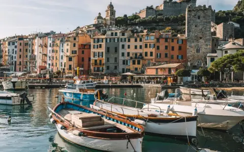 Boats bob in the harbor of a colorful Italian Riviera town, with ancient castles overlooking the vibrant buildings.