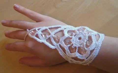 Ett vackert virkat armband i vitt med pärlor, som pryder en hand.