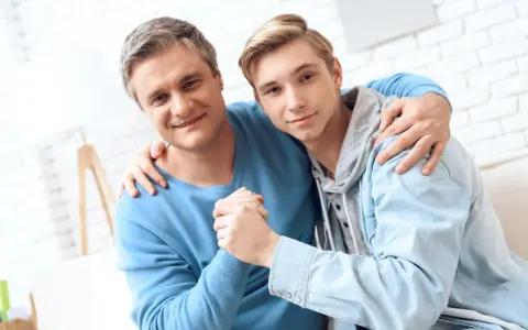 Ojciec obejmuje syna, wspierając go w ważnych życiowych rozmowach.
