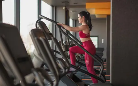 Frau macht ein Stairmaster Workout im Fitnessstudio. Sie trägt ein rotes Sportoutfit und trainiert intensiv.