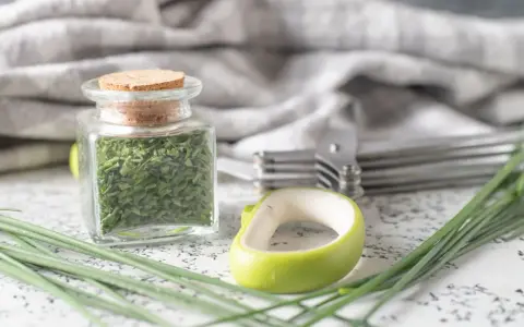A jar filled with dried chives, showcasing how to dry chives for long-term storage. Fresh chives and kitchen tools are nearby.