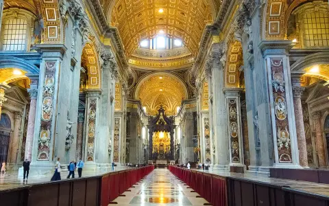 Interior of a grand basilica in Rome, with ornate golden ceilings, marble columns, and a long aisle lined with red velvet.
