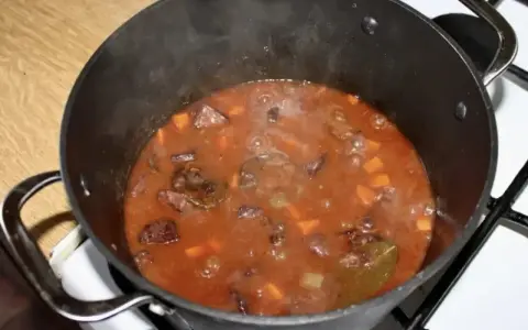 Gorący gulasz z dzika po myśliwsku bulgocze w garnku. Aromatyczny sos z kawałkami mięsa i warzyw.