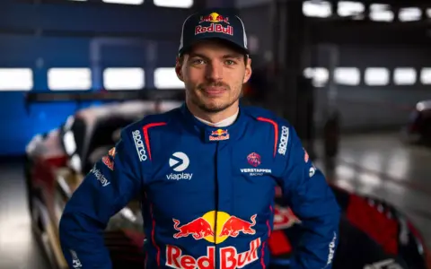 Max Verstappen im Rennanzug, bereit für das 24h Rennen. Sein Blick ist fokussiert, die Red Bull-Logos sind deutlich sichtbar.
