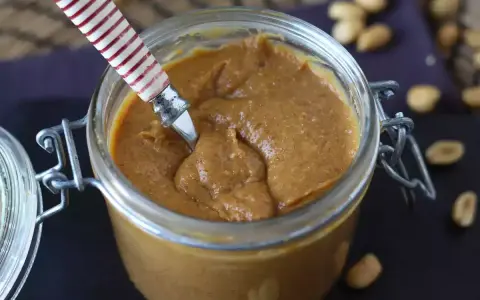 Un pot de praliné cacahuète onctueux, prêt à être dégusté. Quelques cacahuètes parsèment le plan de travail.