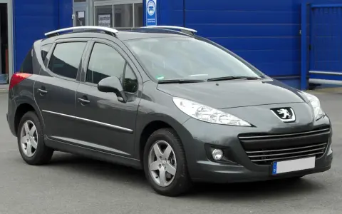 Szary Peugeot 207 1.4 benzyna z relingami dachowymi, zaparkowany przed niebieskim budynkiem.