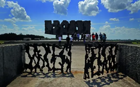 Brama pamięci na terenie byłego obozu Majdanek. Grupa ludzi zwiedza miejsce pamięci.