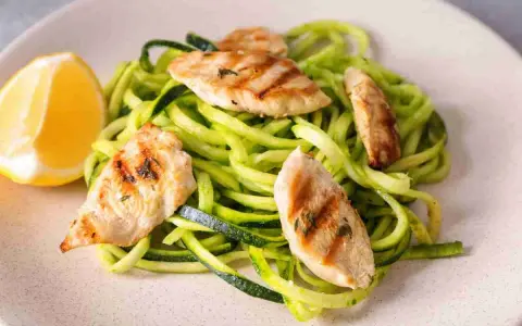Spaghetti di zucchine con straccetti di pollo grigliato e una fetta di limone.