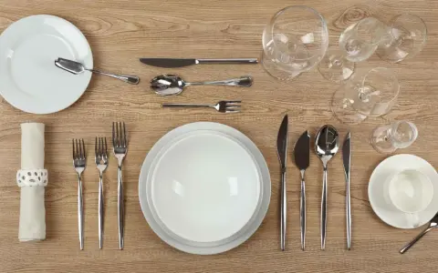 Une table dressée avec un **caractère élégant** : assiettes blanches, couverts en argent, verres à pied et une serviette décorée.