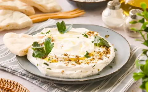 Labneh cremoso con aceite de oliva, za'atar y perejil, servido con pan de pita.