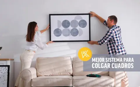 Pareja cuelga un cuadro moderno en pared de pladur. Un taladro descansa sobre el sofá, listo para la tarea.