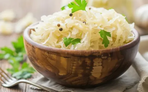 Schüssel mit Sauerkraut, garniert mit Petersilie und Pfefferkörnern. Dieses fermentierte Gericht ist bekannt dafür, dass Sauerkraut gesund ist.