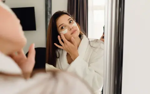 Kobieta w szlafroku nakłada krem pod oczy. Czy retinol to kwas? To pytanie nurtuje wiele osób dbających o cerę.