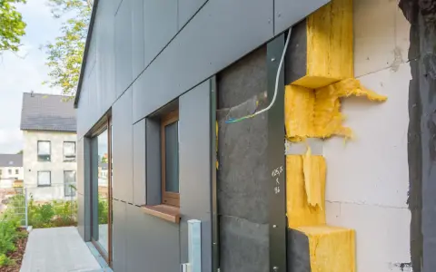 Fassade im Bau: WDVS selber machen mit gelber Steinwolle-Dämmung, die an einer grauen Verkleidung angebracht wird.