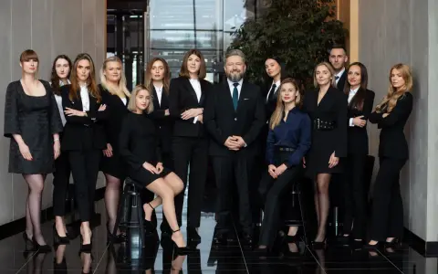 Grupa prawników i adwokatów w eleganckich strojach pozuje do zdjęcia w nowoczesnym wnętrzu.
