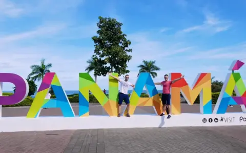 Two men pose with arms outstretched in front of a colorful "PANAMÁ" sign, suggesting Panama is gay friendly and a welcoming destination.