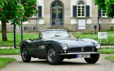 Un elegante BMW descapotable gris, un clásico de Alemania, aparcado frente a un edificio histórico con árboles en flor.
