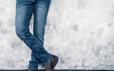 Mężczyzna w jeansach H&M, stojący przy ścianie. Rozmiarówka H&M wypada standardowo, idealnie dopasowana.