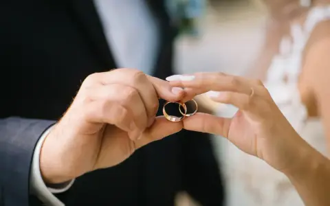 Dłonie pary trzymają obrączki, symbolizujące miłość i wierność. Na której ręce nosi się obrączkę? Zazwyczaj na serdecznym palcu lewej dłoni.