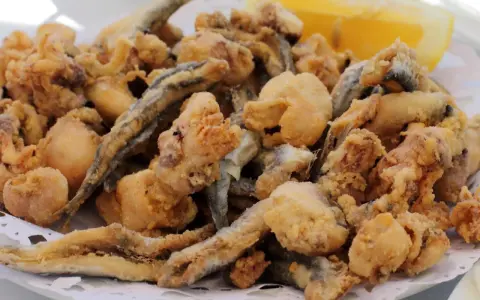 Frito y crujiente pescado en adobo, con trocitos de calamar y una rodaja de limón.