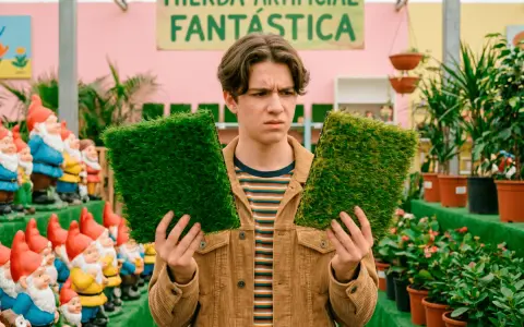 Joven indeciso compara dos tipos de césped artificial, rodeado de gnomos y plantas.