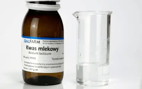 Butelka z napisem "Kwas mlekowy" i zlewka z płynem. Czy kwas mlekowy jest szkodliwy? Zależy od stężenia i zastosowania.