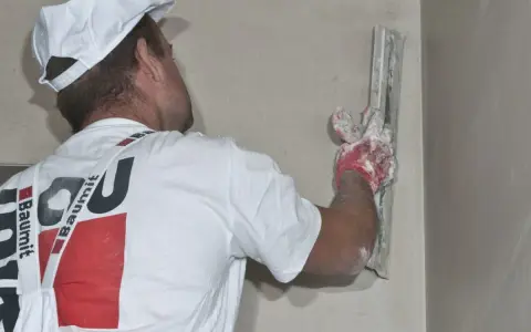 Pracownik nakłada tynki gipsowe czy cementowo wapienne na ścianę, używając kielni.