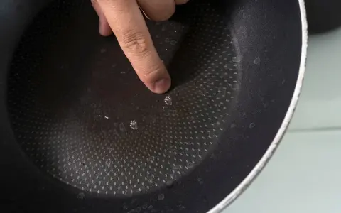 Palec wskazujący na uszkodzoną powłokę patelni. Czas na recykling i pytanie: gdzie wyrzucić patelnię?